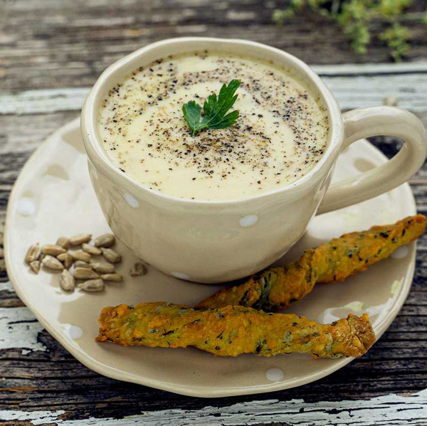KI generiert: Eine Tasse Sahnesuppe mit Pfeffer, dekoriert mit Petersilie, serviert auf Teller mit Brotsticks und Sonnenblumenkernen.