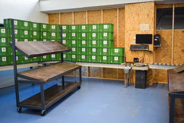 KI generiert: Grüner Lagerraum mit Kisten, zwei Rollwagen, Computerstation an der Wand.