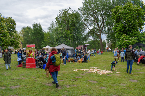 KI generiert: Eine Outdoor-Veranstaltung mit Ständen, Menschen, und Spielen im Park. Text: nicht lesbar.