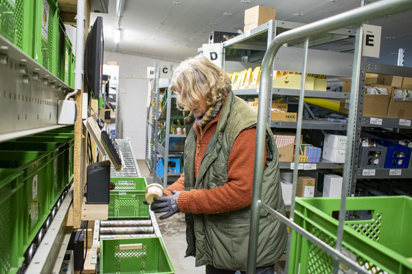 KI generiert: Person in Lager sortiert Waren in grüne Kisten. Regale im Hintergrund.