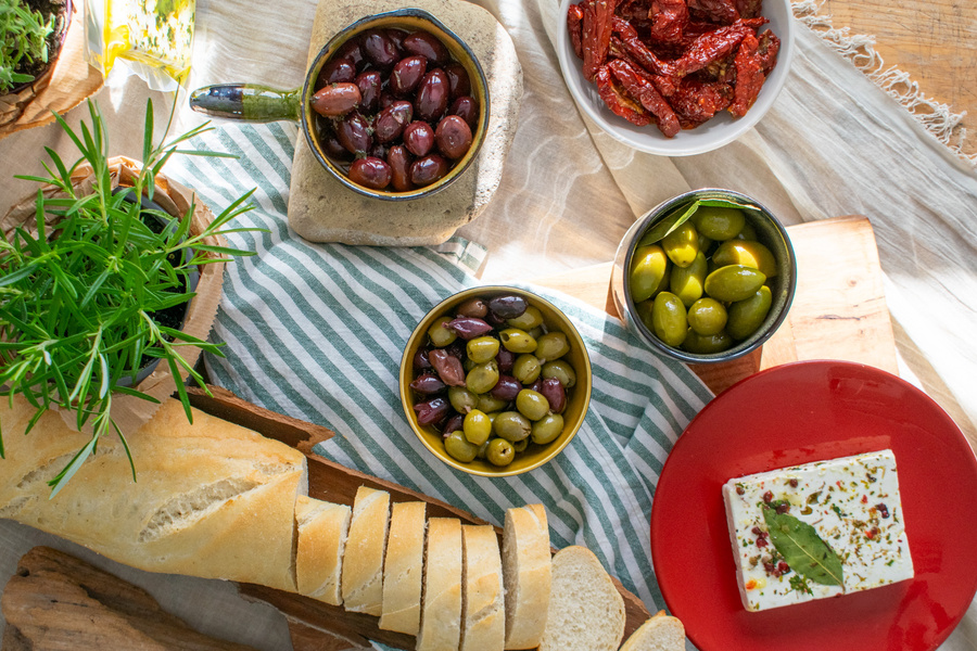 KI generiert: Mediterrane Vorspeisenplatte mit Oliven, getrockneten Tomaten, Baguette, Frischkäse und frischen Kräutern.