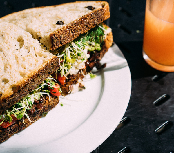 KI generiert: Ein gefülltes Sandwich auf einem Teller neben einem Glas Saft.