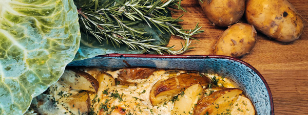 KI generiert: Ein Kartoffelgericht in einer Auflaufform mit Kräutern, Kohlblatt und Kartoffeln im Hintergrund.