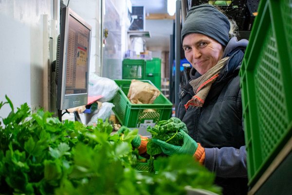 KI generiert: Person sortiert frisches Gemüse in Kisten, konzentriert sich auf Kräuter. Ein Monitor ist im Hintergrund sichtbar.
