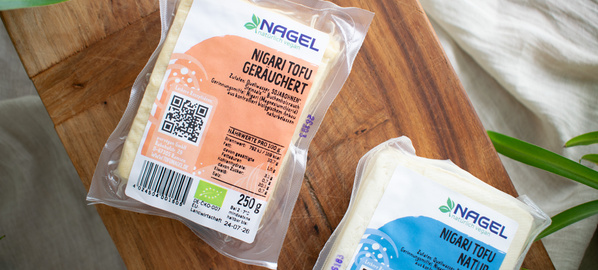 KI generiert: Zwei Packungen Nigari Tofu auf einem Holzbrett, eine geräuchert und eine natur.