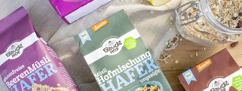 KI generiert: Verschiedene Bauckhof-Müsli-Verpackungen auf einem Tisch, darunter „Glutenfreies BeerenMüsli“ und „Hofmischung Hafer“.